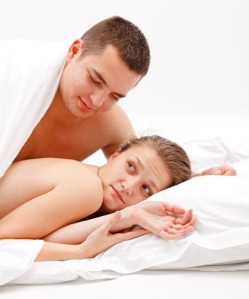 Young, naked couple in bed, the man leaning over the woman